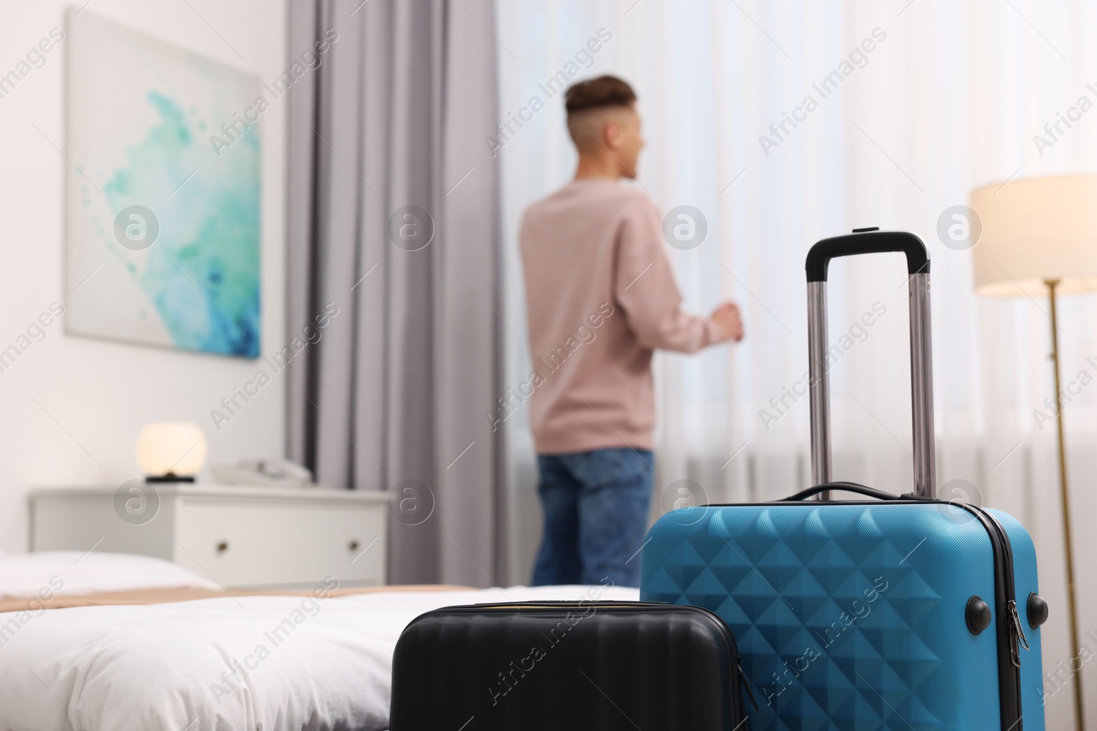 Photo of Guest opening curtains in stylish hotel room, focus on suitcases