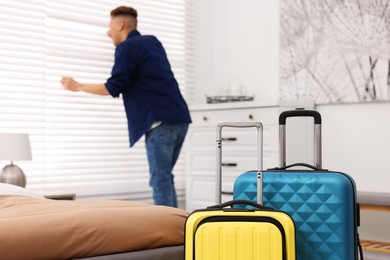 Photo of Guest looking through blinds in stylish hotel room, focus on suitcases