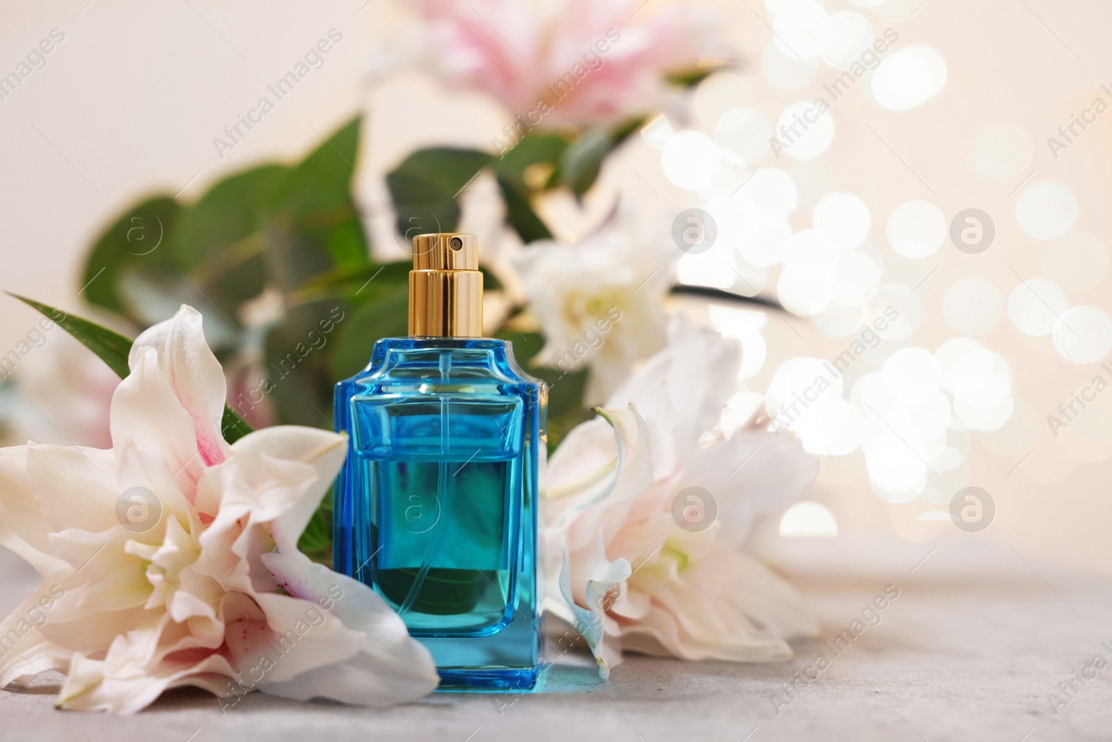 Photo of Bottle of perfume and beautiful lily flowers on table against beige background with blurred lights, closeup