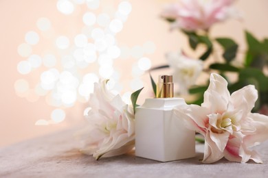 Photo of Bottle of perfume and beautiful lily flowers on table against beige background with blurred lights, closeup. Space for text