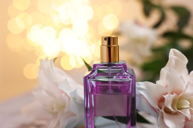 Photo of Bottle of perfume and beautiful lily flowers against beige background with blurred lights, closeup