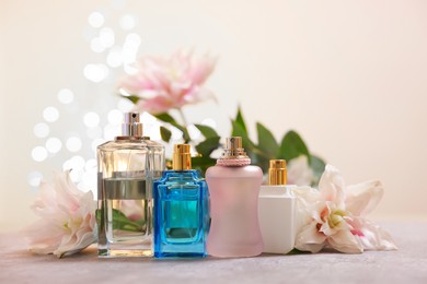 Photo of Perfume bottles and bouquet of beautiful lily flowers on table against beige background with blurred lights, closeup