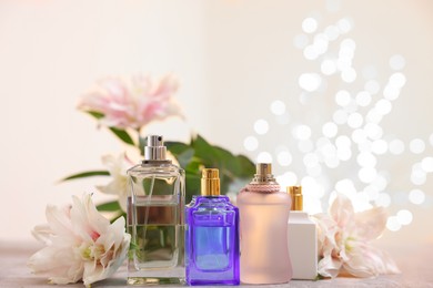 Photo of Perfume bottles and bouquet of beautiful lily flowers on table against beige background with blurred lights, closeup