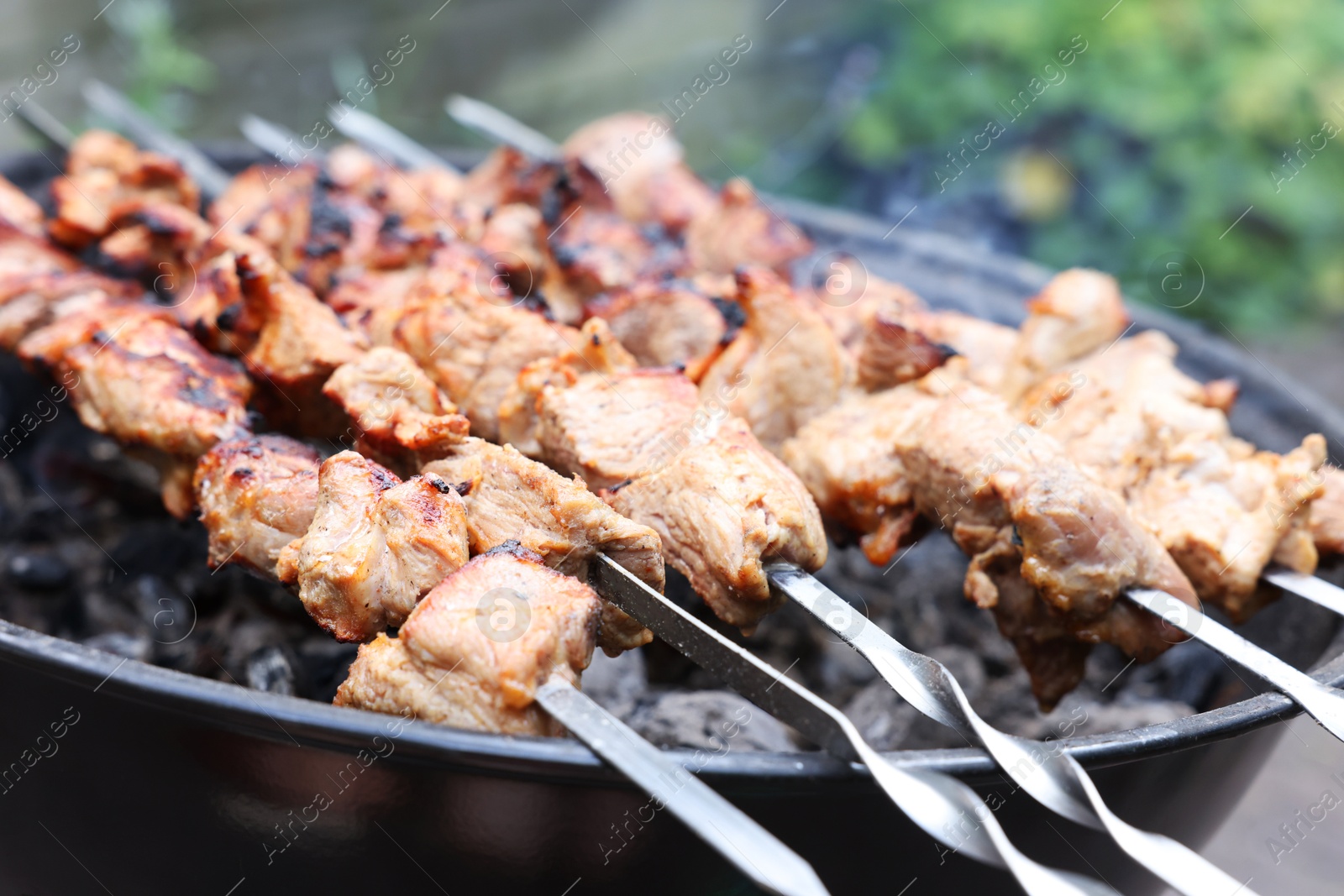 Photo of Cooking delicious kebab on metal brazier outdoors, closeup