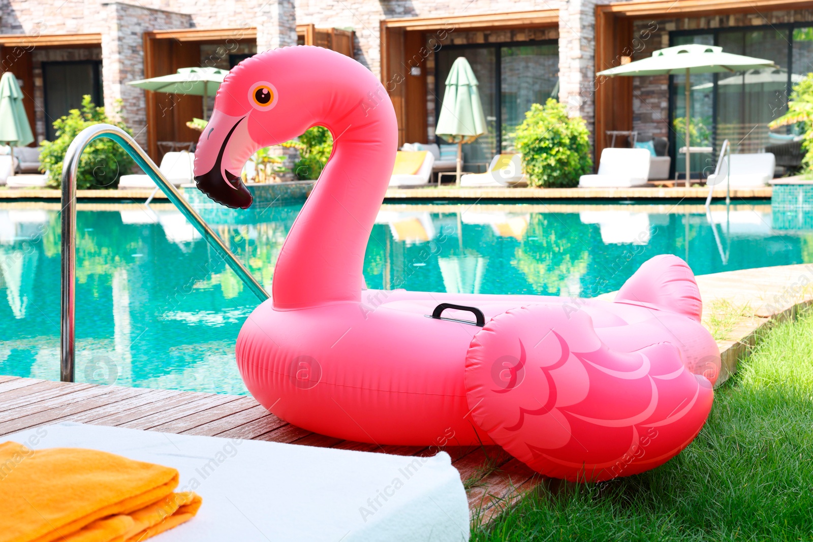 Photo of Float in shape of flamingo on wooden deck near swimming pool and sunbeds at luxury resort