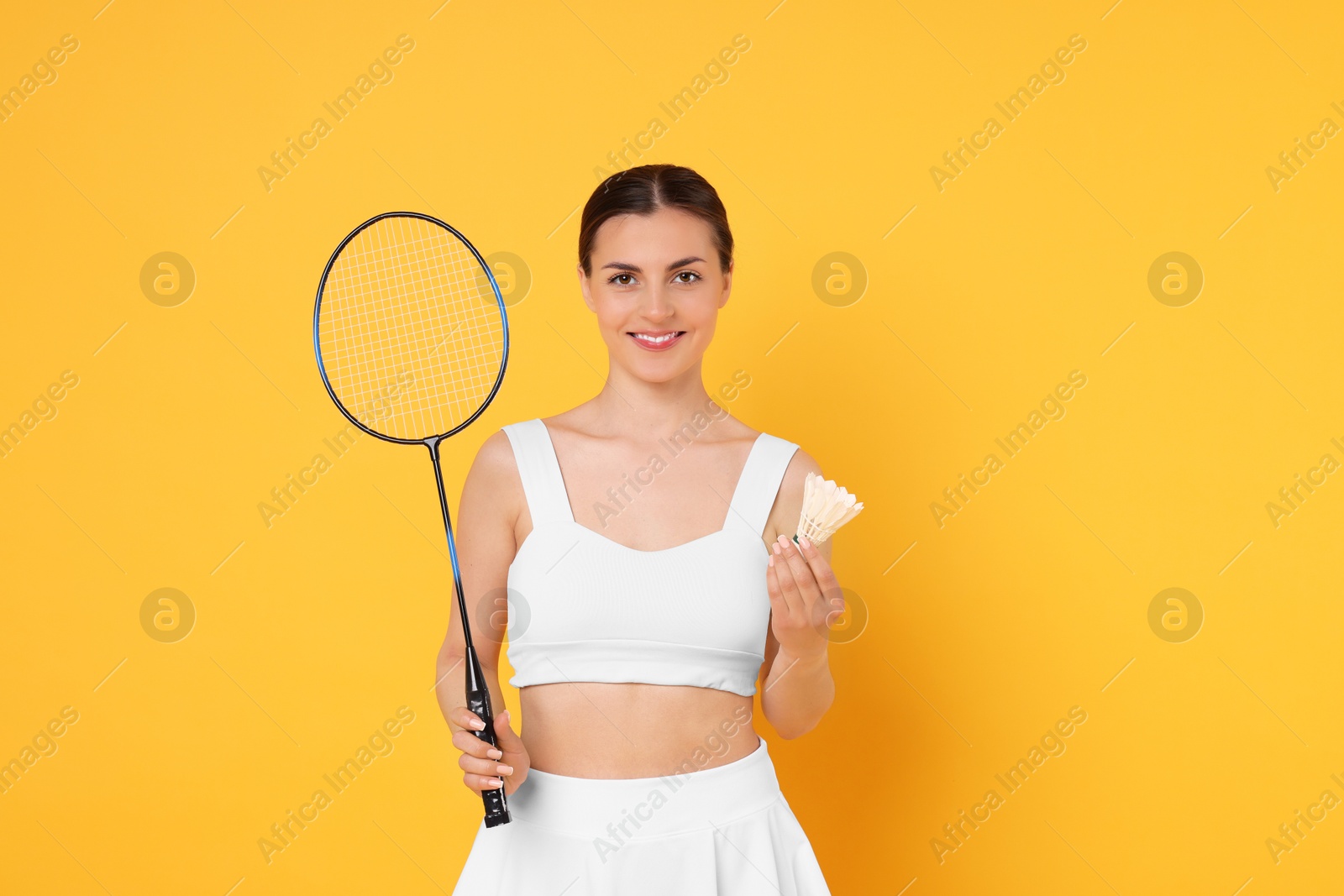 Photo of Young woman with badminton racket and shuttlecock on orange background