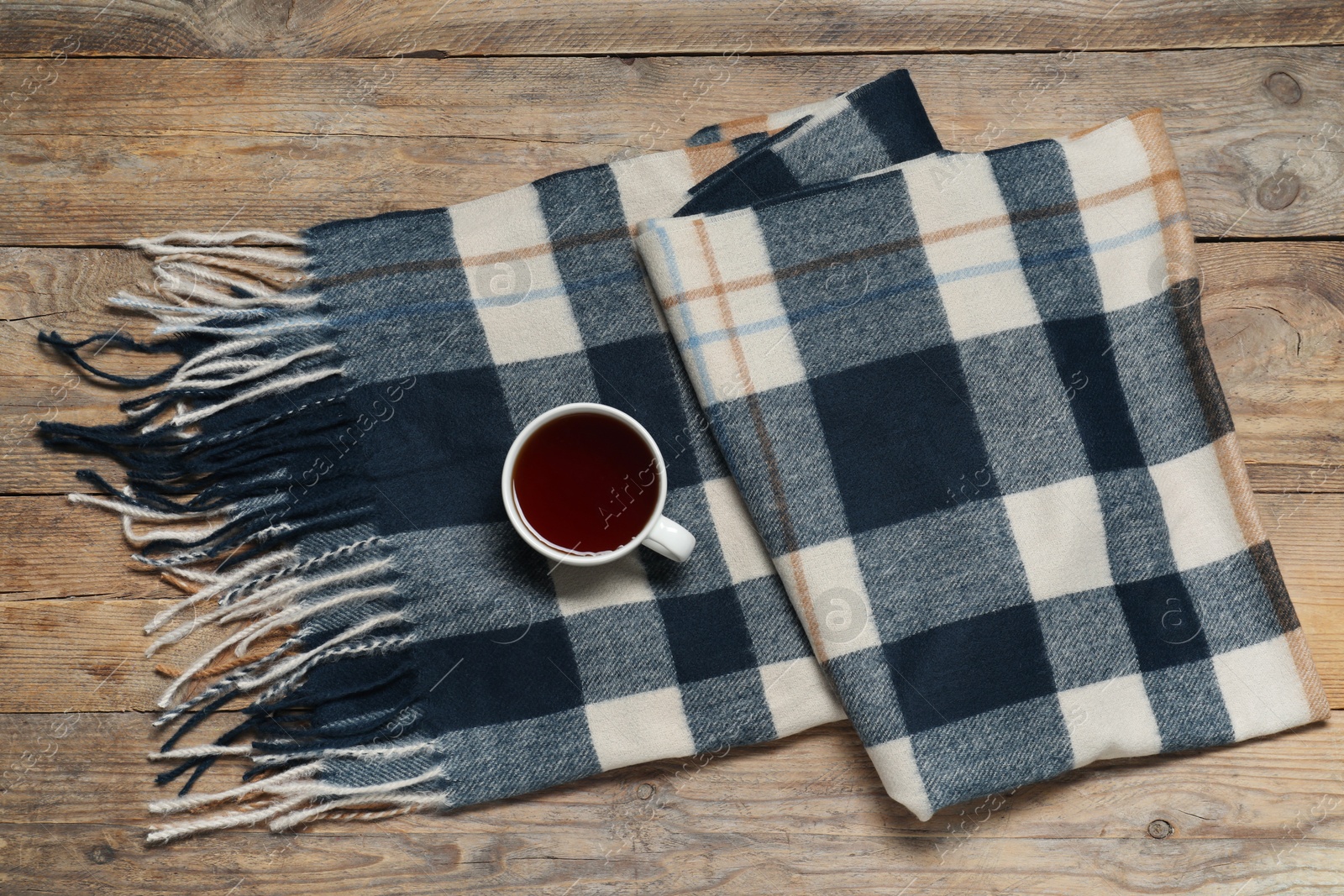 Photo of Soft checkered scarf and tea on wooden table, top view