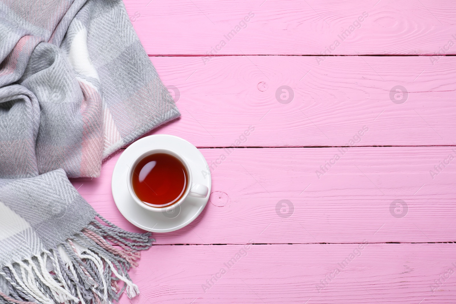 Photo of Checkered scarf and tea on pink wooden table, top view. Space for text