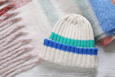 Soft scarf and knitted hat on wooden table, top view