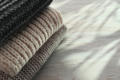 Stack of knitted scarfs on wooden table, space for text