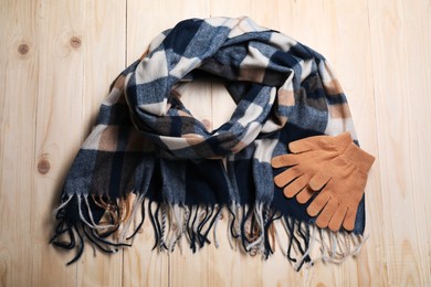 Soft checkered scarf and gloves on wooden table, top view