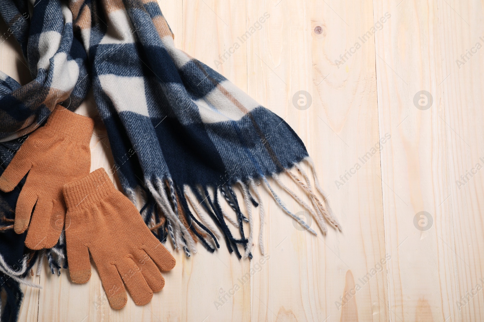 Photo of Soft checkered scarf and gloves on wooden table, top view. Space for text