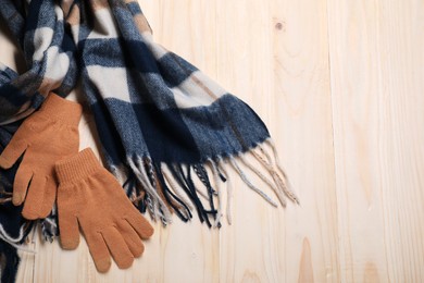 Photo of Soft checkered scarf and gloves on wooden table, top view. Space for text