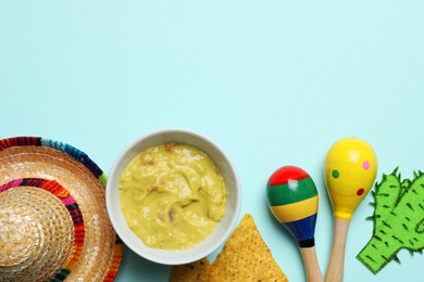 Mexican sombrero hat, guacamole, nachos chips, maracas and paper cactus on light blue background, flat lay. Space for text
