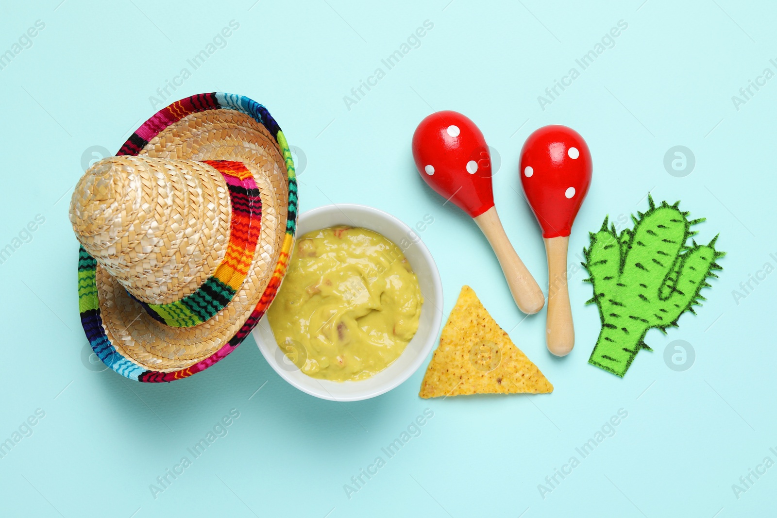 Photo of Mexican sombrero hat, guacamole, nachos chip, maracas and paper cactus on light blue background, flat lay