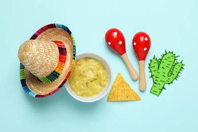 Mexican sombrero hat, guacamole, nachos chip, maracas and paper cactus on light blue background, flat lay