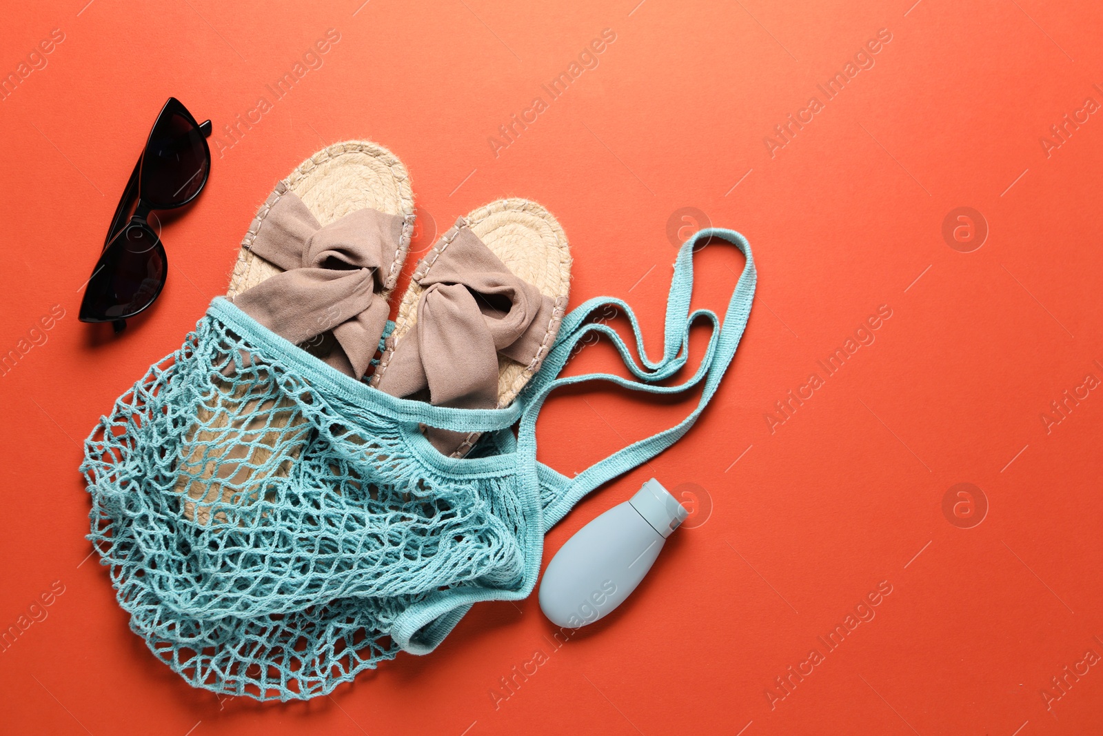 Photo of String bag, sunglasses, slippers and cosmetic product on coral background, top view