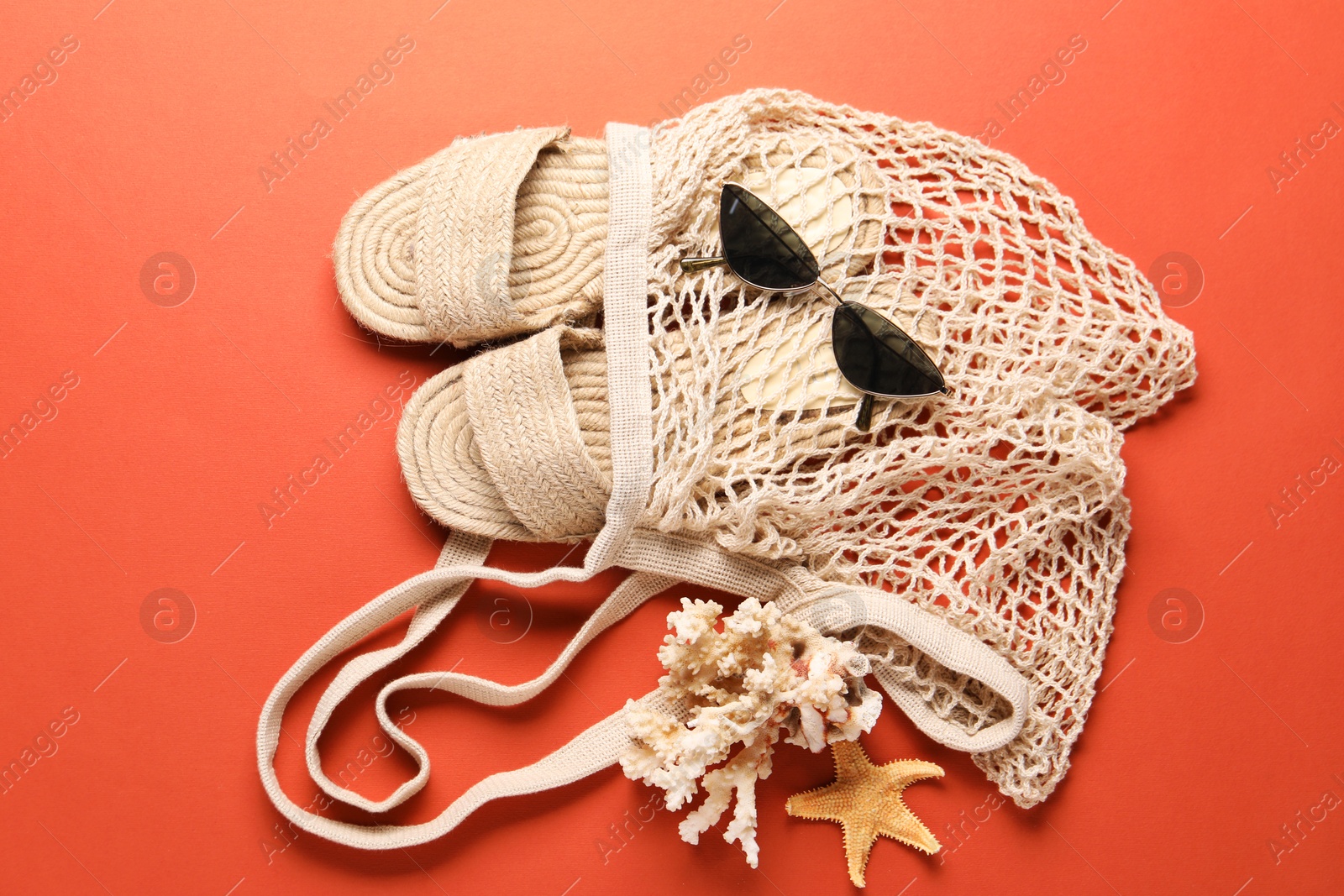 Photo of String bag, sunglasses, slippers, starfish and coral on color background, top view