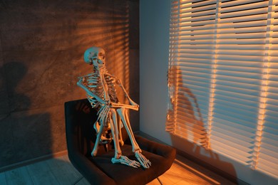 Photo of Waiting concept. Human skeleton sitting in armchair indoors, space for text