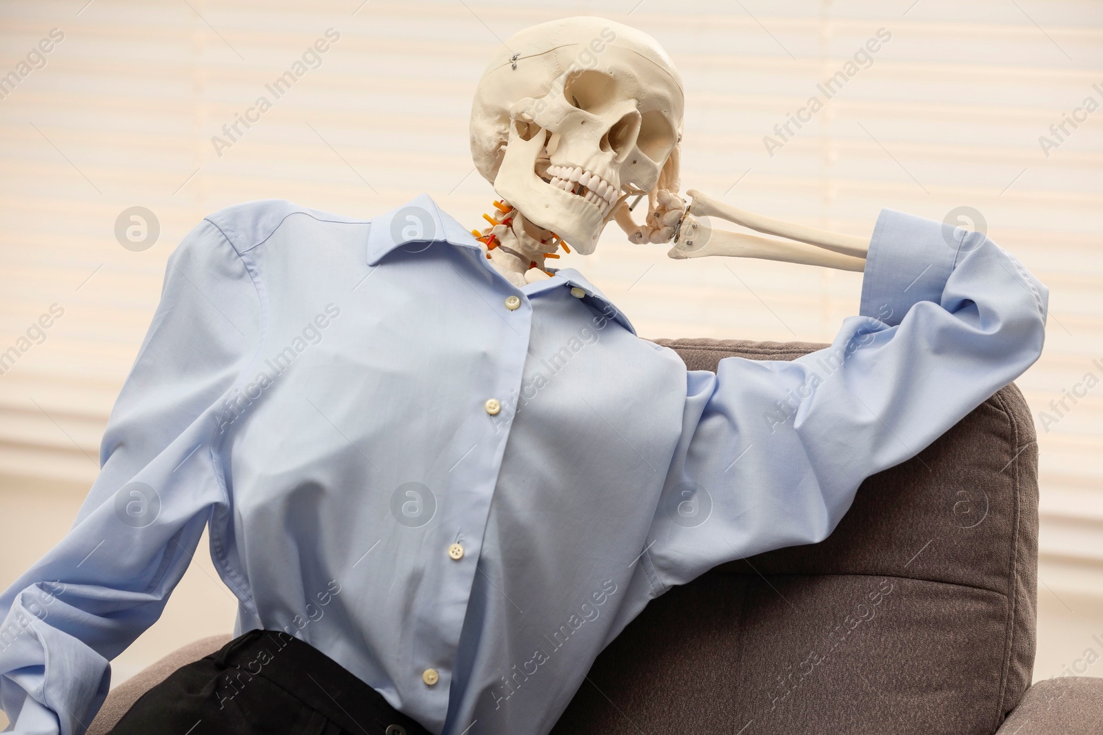 Photo of Waiting concept. Human skeleton sitting in armchair at office