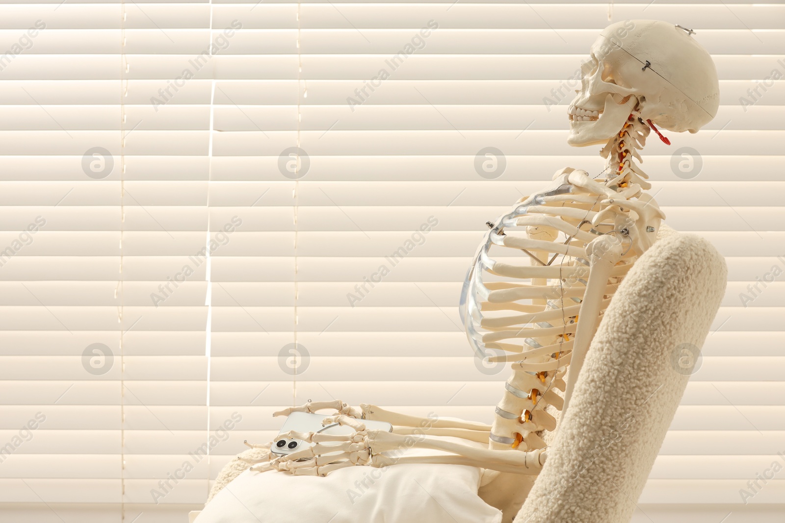 Photo of Waiting concept. Human skeleton sitting in armchair with smartphone indoors, space for text