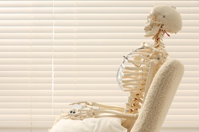 Photo of Waiting concept. Human skeleton sitting in armchair with smartphone indoors, space for text