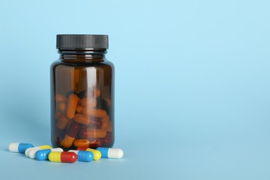 Photo of Antibiotic pills and bottle on light blue background, space for text. Medicinal treatment