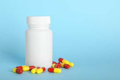 Photo of Antibiotic pills and bottle on light blue background, space for text. Medicinal treatment