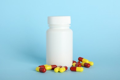 Photo of Antibiotic pills and bottle on light blue background. Medicinal treatment