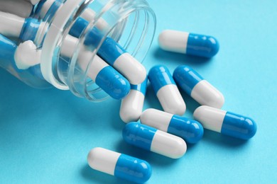 Scattered antibiotic pills and bottle on light blue background, closeup. Medicinal treatment