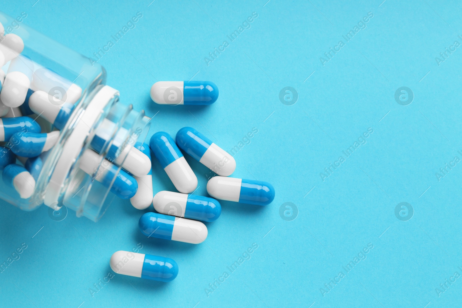 Photo of Scattered antibiotic pills and bottle on light blue background, top view with space for text. Medicinal treatment