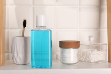 Photo of Bottle of mouthwash, toothbrush, cotton buds and pads on white shelf in bathroom