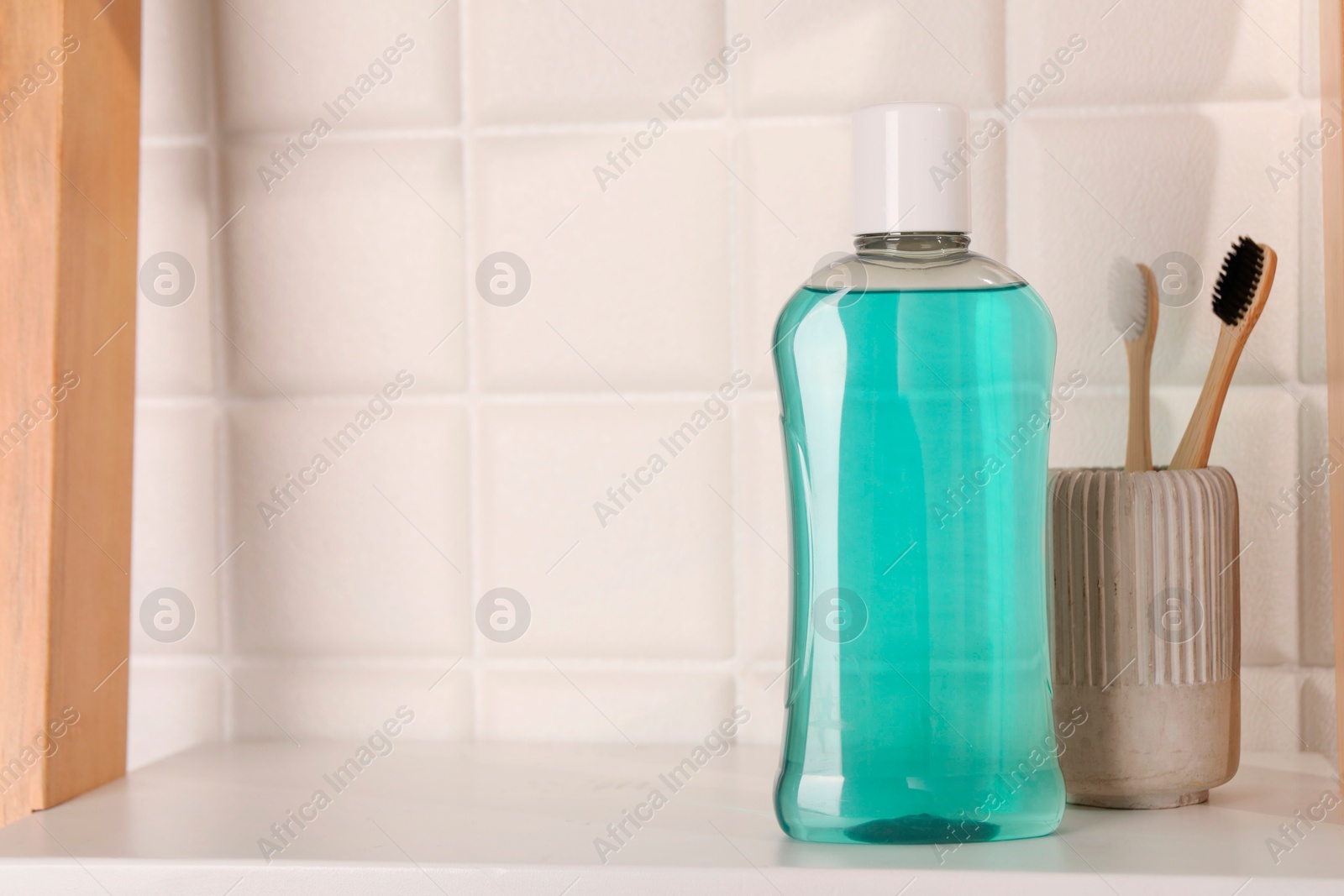 Photo of Bottle of mouthwash and toothbrushes on white shelf in bathroom, space for text