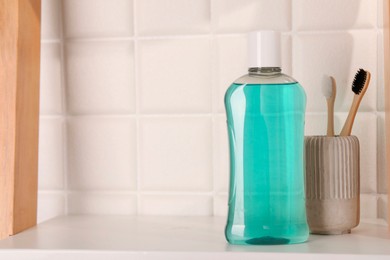 Photo of Bottle of mouthwash and toothbrushes on white shelf in bathroom, space for text