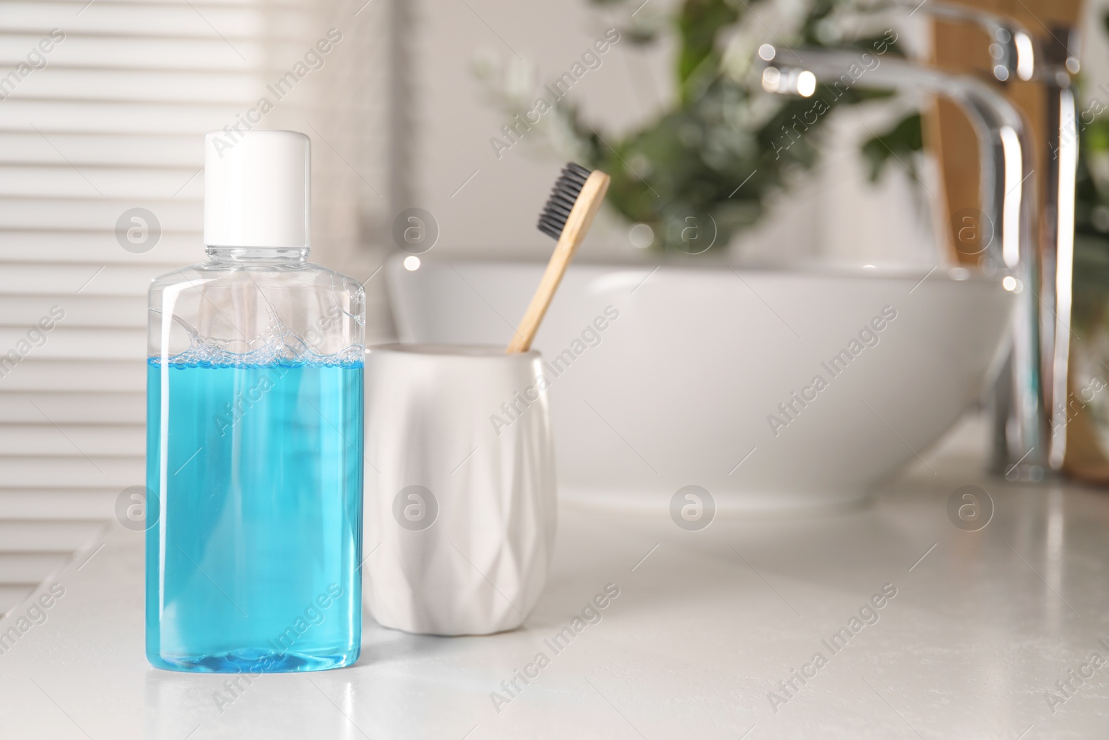 Photo of Bottle of mouthwash and toothbrush on white countertop in bathroom