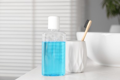 Photo of Bottle of mouthwash and toothbrush on white countertop in bathroom