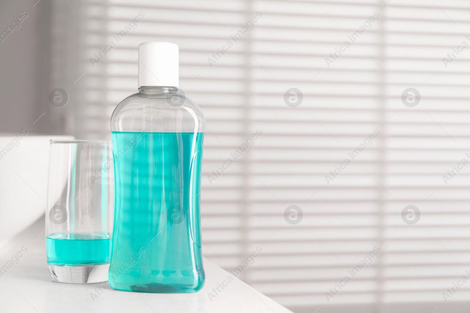 Photo of Bottle and glass of mouthwash on white countertop in bathroom, space for text