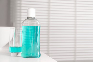 Bottle and glass of mouthwash on white countertop in bathroom, space for text