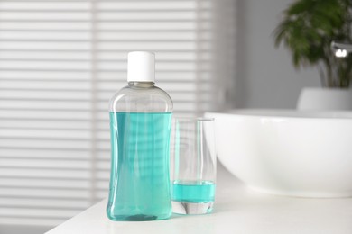 Photo of Bottle and glass of mouthwash on white countertop in bathroom