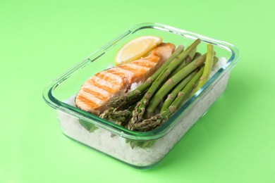 Photo of Healthy meal. Fresh asparagus, salmon and rice in glass container on green background