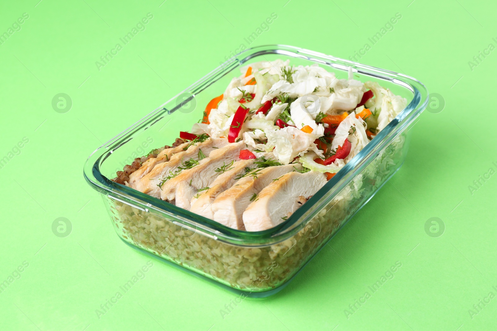 Photo of Healthy meal. Fresh salad, chicken and buckwheat in glass container on green background