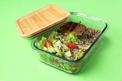 Photo of Healthy meal. Fresh salad, cutlet and buckwheat in glass container on green background