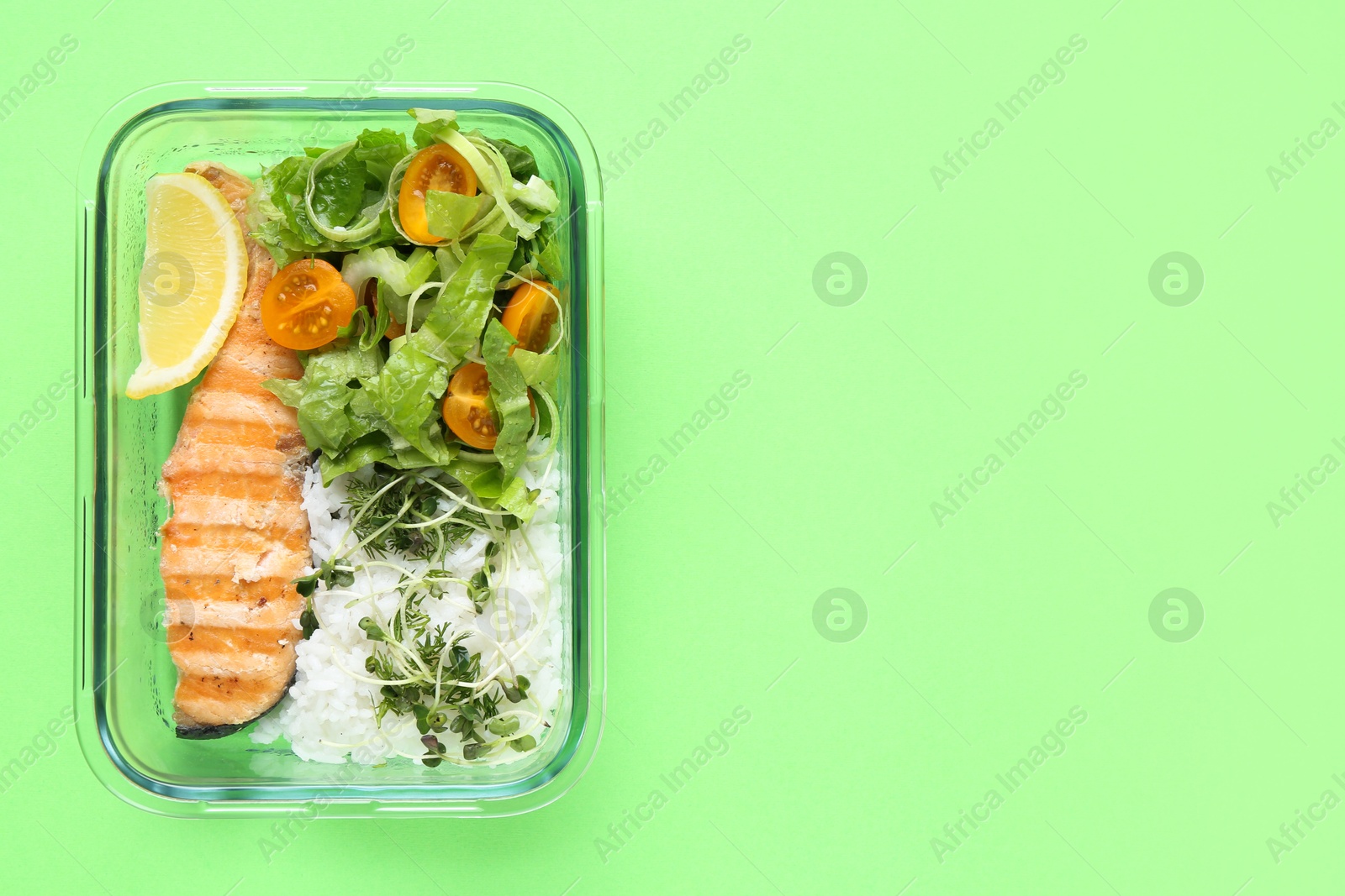 Photo of Healthy meal. Fresh salad, salmon and rice in glass container on green background, top view. Space for text