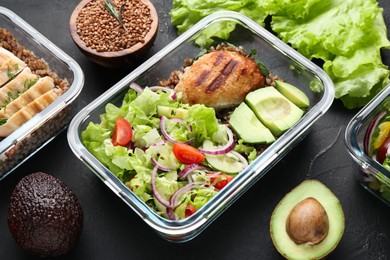 Photo of Healthy meal. Fresh salad, avocado, cutlet and buckwheat in glass container near other products on black table
