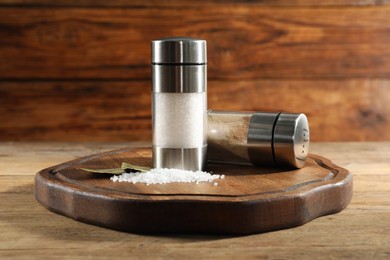 Photo of Salt and pepper shakers with bay leaves on wooden table