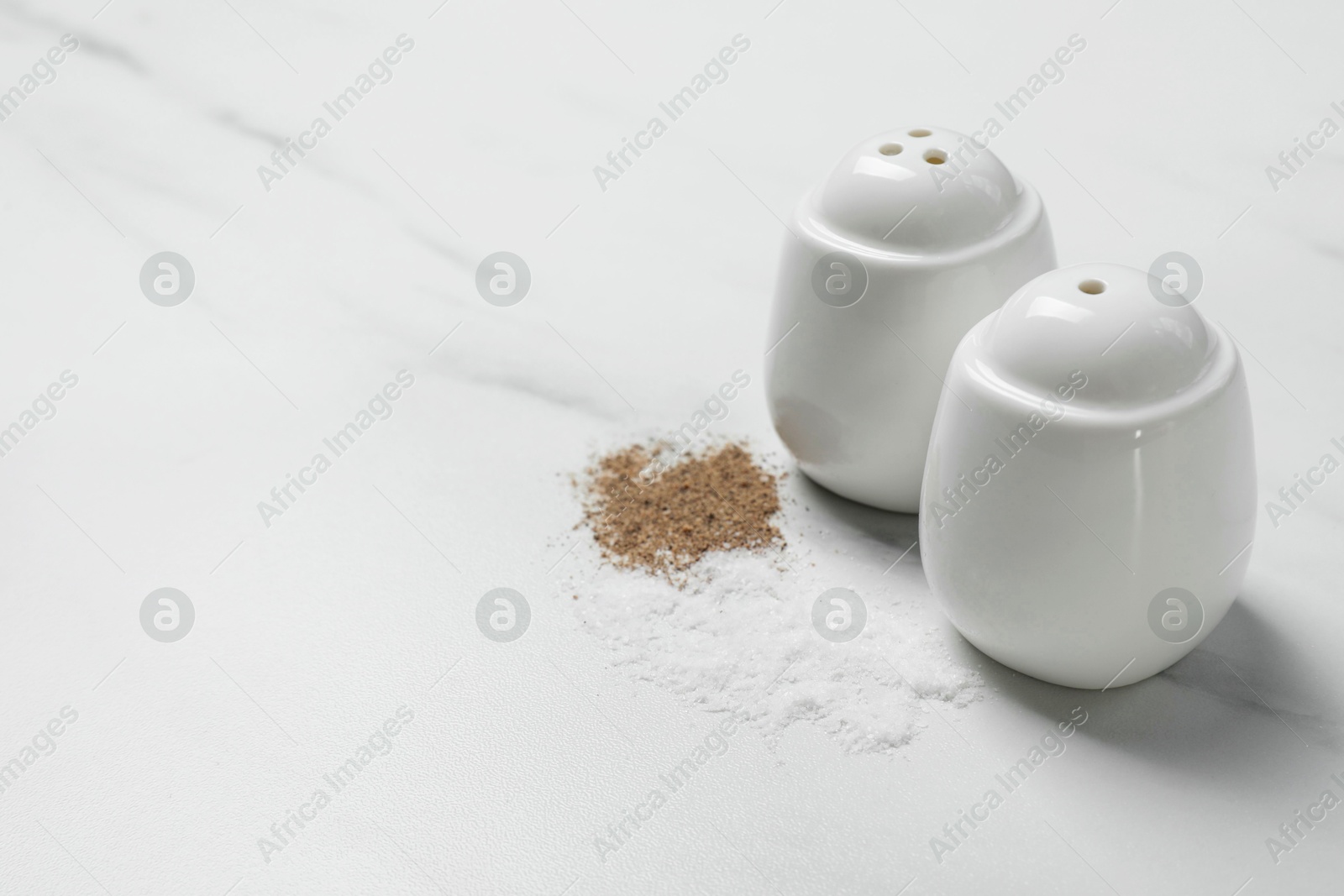 Photo of Salt and pepper shakers on white marble table, space for text