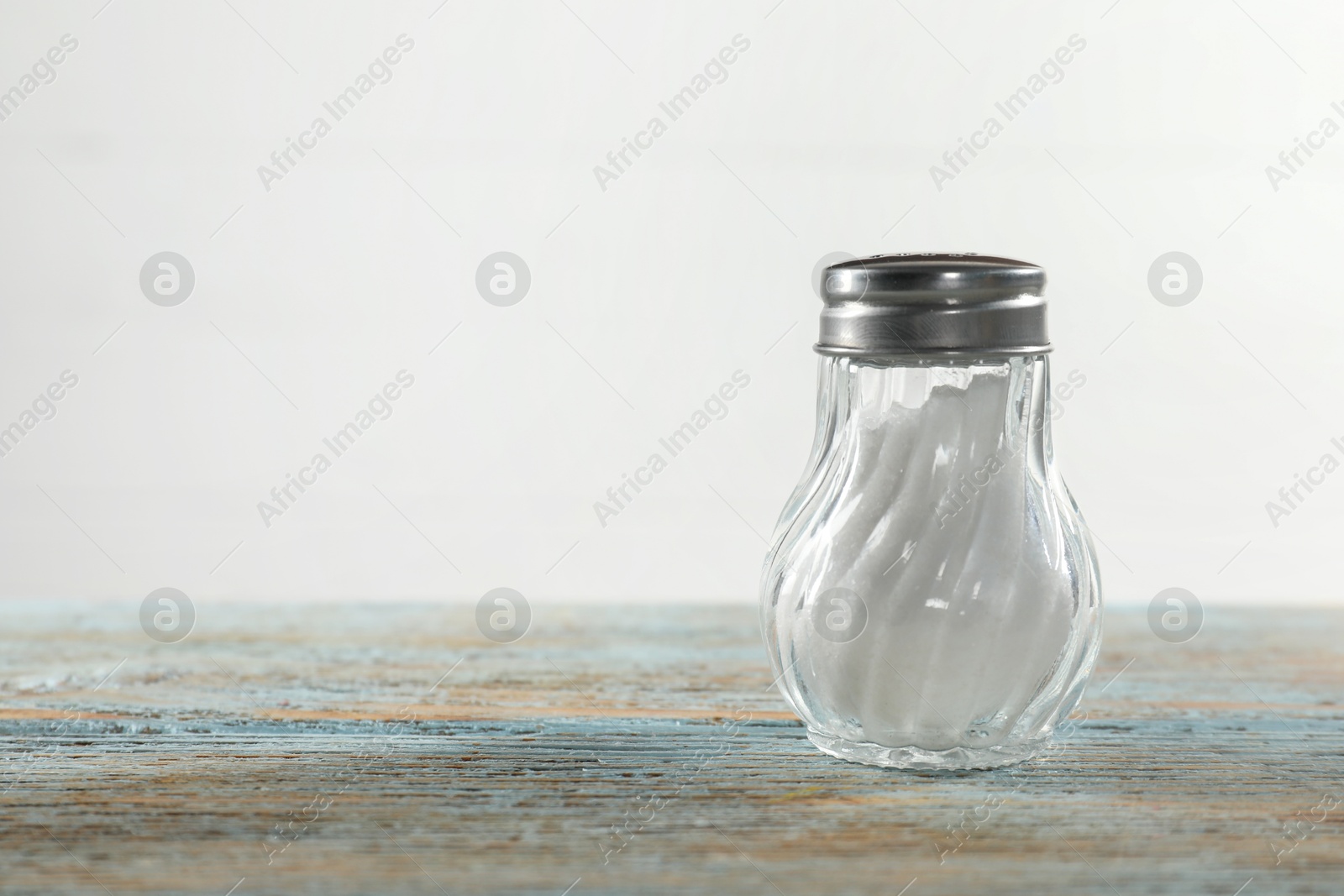 Photo of Salt shaker on light blue wooden table, closeup. Space for text