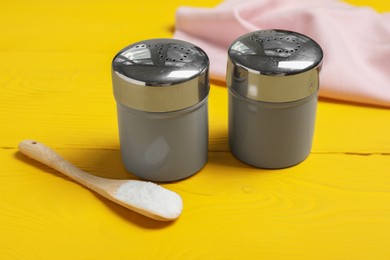 Photo of Spice shakers with salt on yellow wooden table