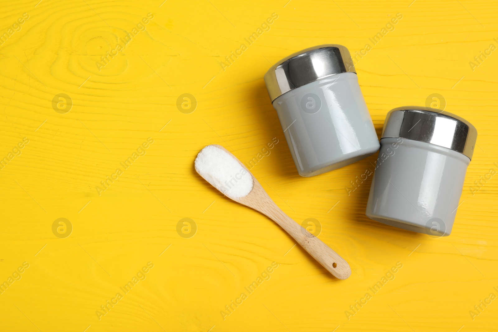 Photo of Spice shakers with salt on yellow wooden table, flat lay. Space for text