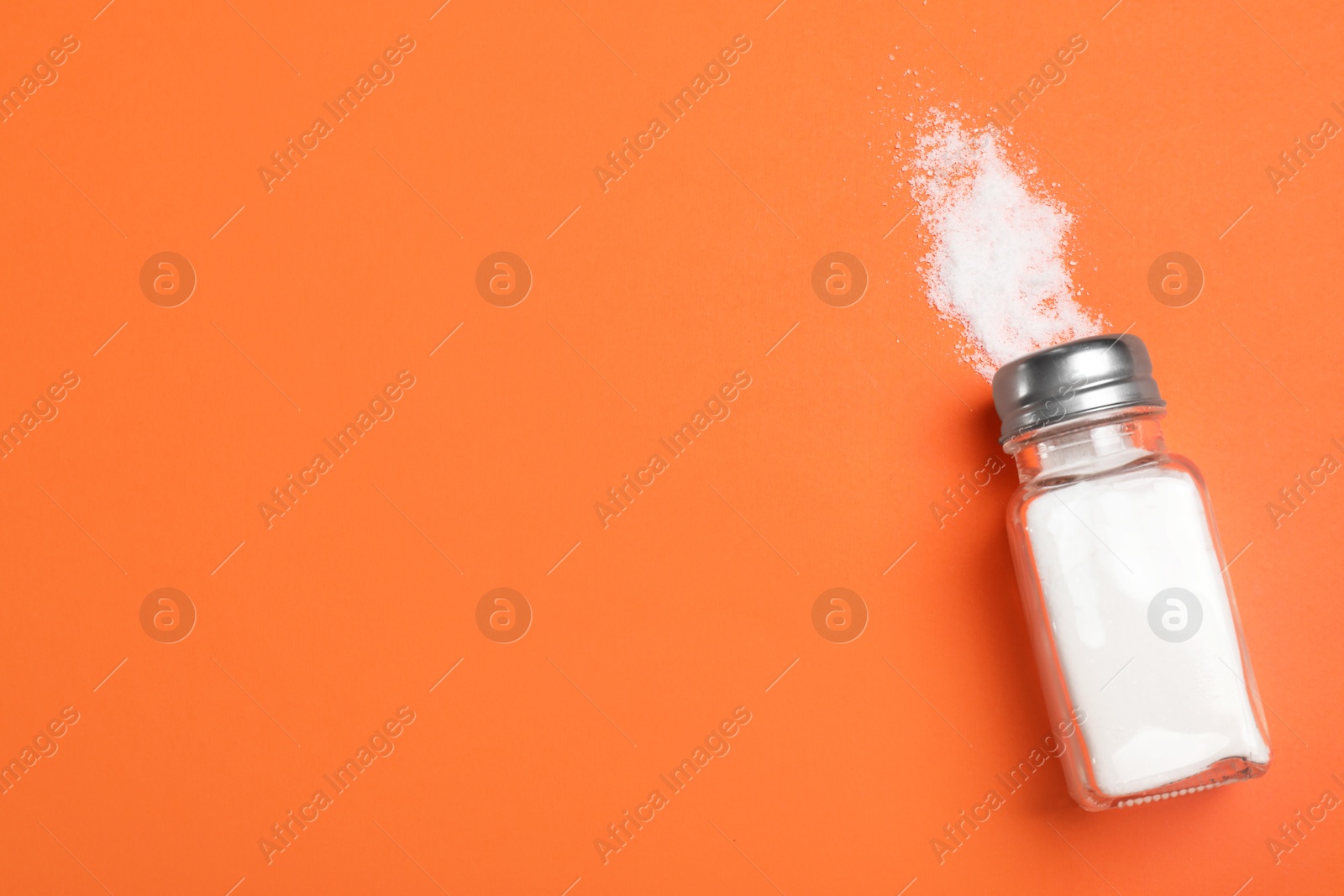 Photo of Salt shaker on orange table, top view. Space for text